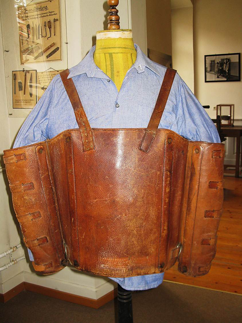 Leibfessel aus Leder, genannt Englisches Hemd, welches das Anliegen der Arme an den Körper erzwingt, auf einem blauen Häftlingshemd an einer gelben Kleiderpuppe