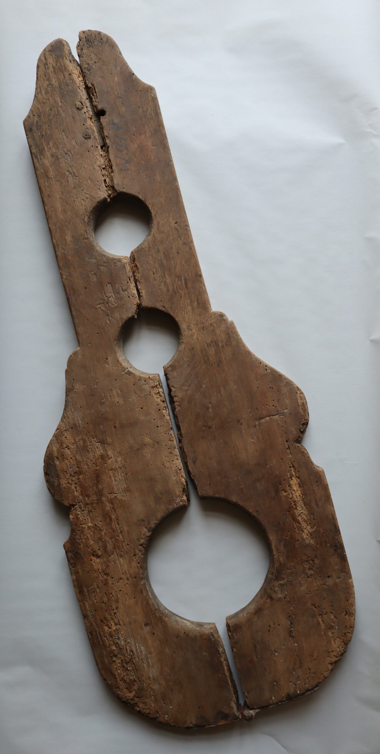 zweiteilige Schandgeige aus Holz, die von der Form her an das gleichnamige Musikinstrument erinnert, mit einer großen Aussparung für den Kopf und zwei kleinen für die Hände, als Objekt im Strafvollzugsmuseum ausgestellt