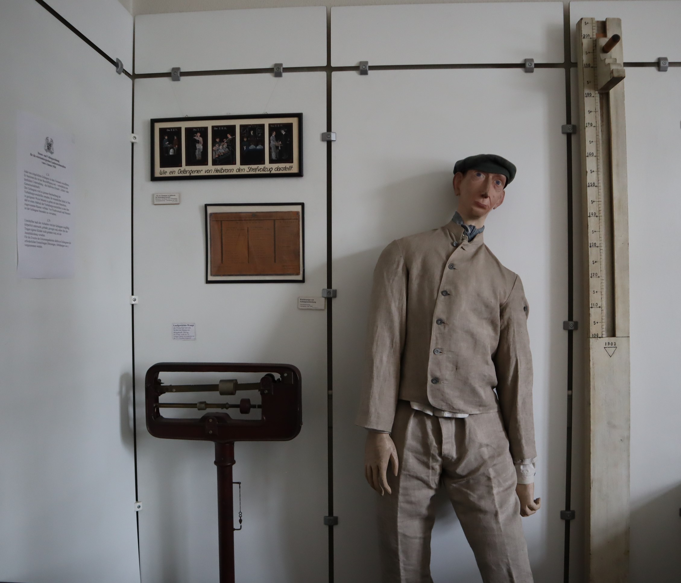 Ecke des Ausstellungsraumes in der Lehrmittelsammlung des Strafvollzugsmuseums mit einer Waage, einem Größenmesser und einer Puppe mit Sträflingskleidung aus der Landesstrafanstalt der 30er