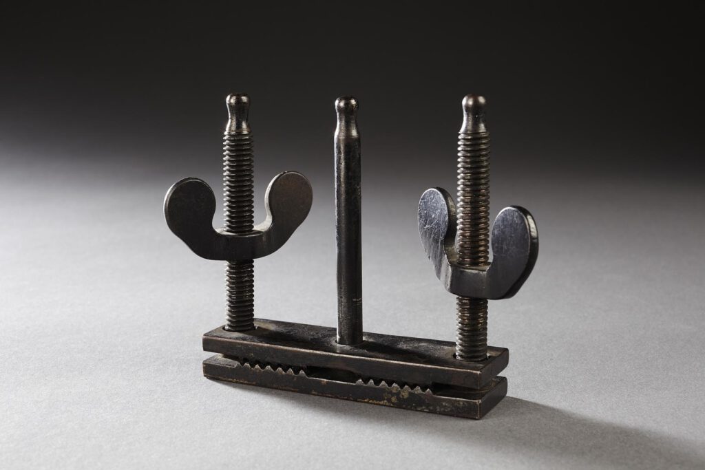 ein Paar Daumenschrauben, bestehend aus zwei Flügelkopfschrauben und einer einfachen Schraube in der Mitte, die auf einem Metallblättchen angebracht sind
