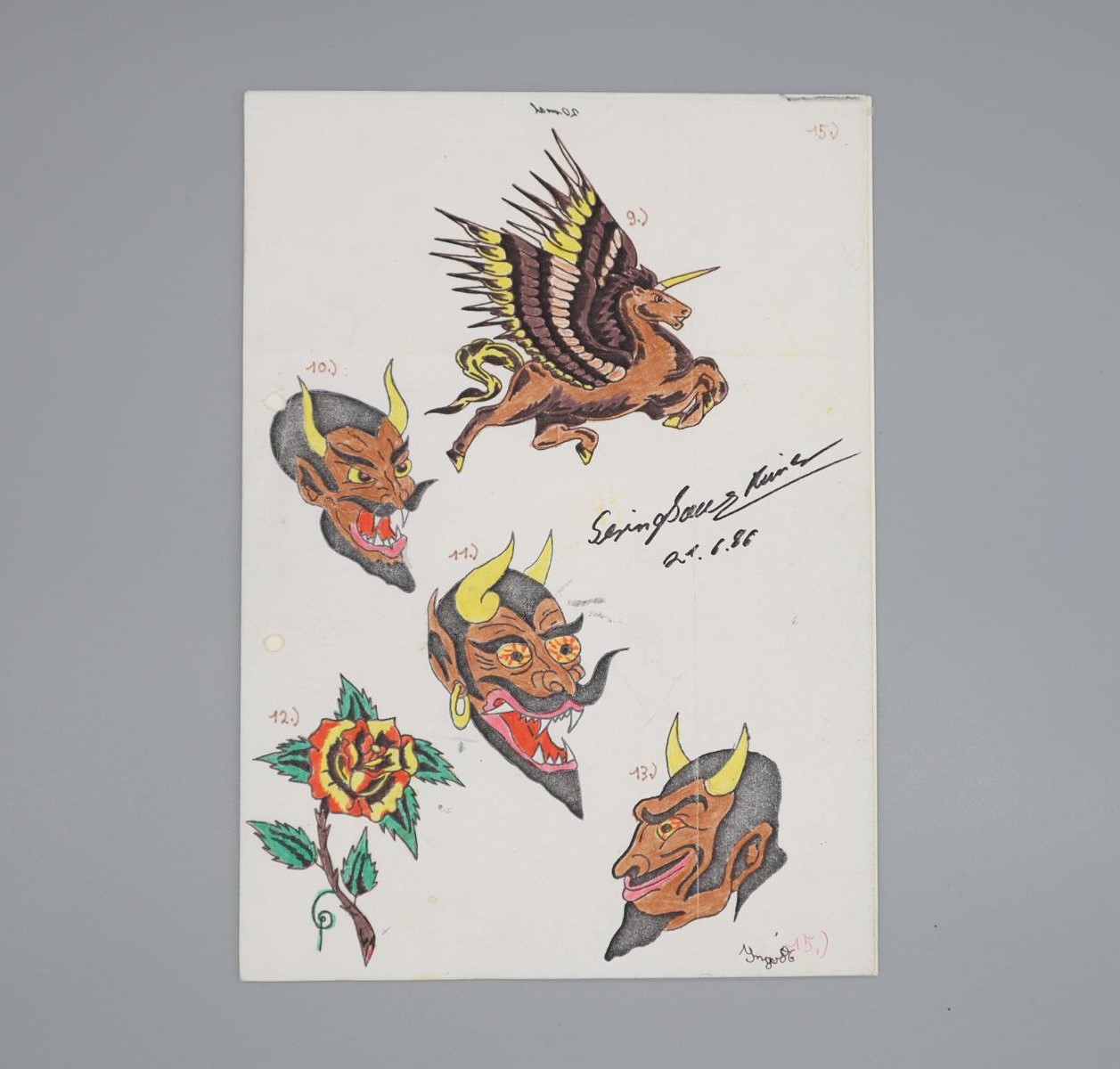 Tätowiervorlage auf DNA4-Blatt mit fünf farbigen Motiven, einem geflügelten Einhorn, drei verschiedenen Teufelsköpfen und einer Rose. Die Vorlage wurde 1988 in der Vollzugsanstalt Luswigsburg gefunden und ist mittlerweile Objekt des Strafvollzugsmuseums.