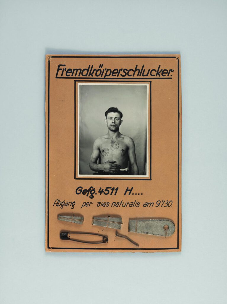 Schautafel aus der Lehrmittelsammlung des Strafvollzugsmuseums über den Fremdkörperschlucker Gefangener 4511 H., der fünf Gegenstände, darunter eine schwarze Büroklammer, verschluckte, die am 9.7.1930 vias naturalis wieder abgingen