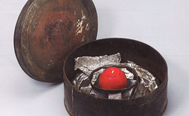 Selbstgebauter Pizzaofen der RAF aus einer alten Keksdose, mit Alufolie ausgelegt und mit einem Metallgestell, auf dem eine rote Kerze angebracht ist, als Objekt im Strafvollzugsmuseum ausgestellt